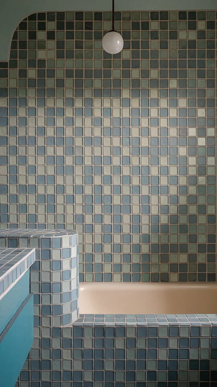 Submerged in serenity: This mid-century modern bathroom's stunning sea glass bathroom backsplash, crafted from large format tile, transforms the bathtub surround and shower tile into a tranquil oasis. The large tile walls create a truly immersive experience, showcasing trending bathroom tile ideas and offering a unique take on mosaic bathroom ideas.
