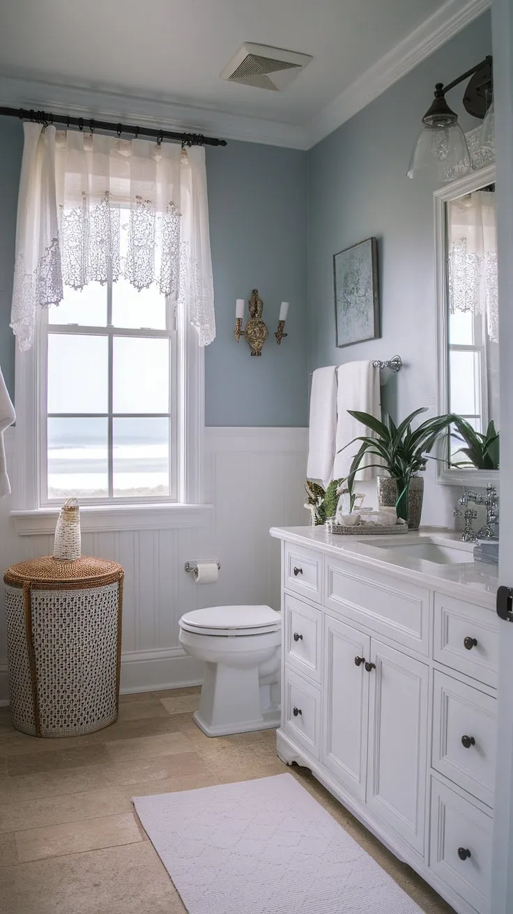 This coastal bathroom design effortlessly blends chic coastal style with rustic farmhouse details.  Consider this bathroom remodel coastal farmhouse inspiration for your own beach home bathroom ideas.  From the light blue walls to the white vanity and ocean view, this half bath coastal decor is the epitome of beach guest bathroom ideas, offering a stylish and relaxing space.