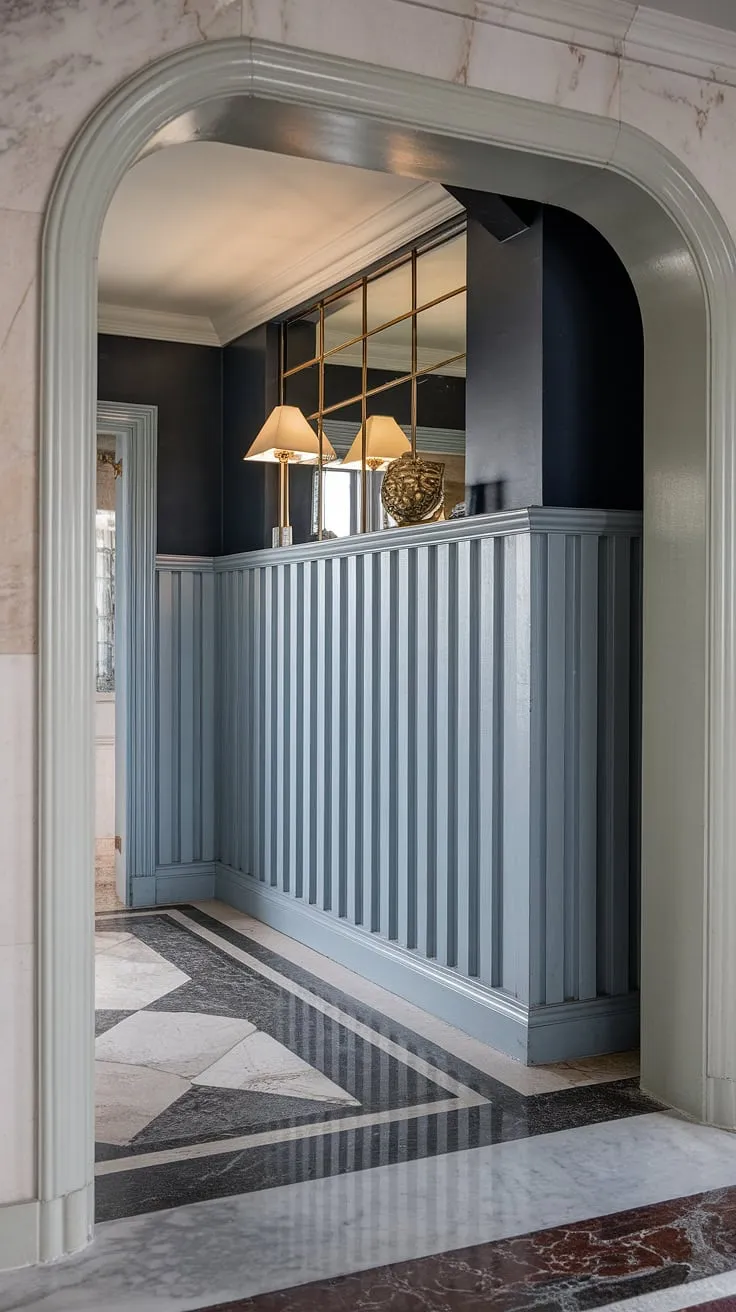 Step into elegance with this stunning art deco entryway wainscoting. Half-panel wainscoting extends to the ceiling, showcasing exquisite wainscoting ideas for high ceilings and offering a perfect blend of wainscoting for hallways and foyers. The rich dark blue above complements the geometric marble floor, making it a showstopper of wall trim ideas.