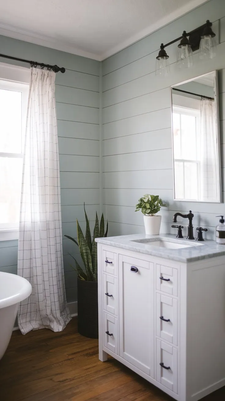 A serene modern farmhouse bathroom boasts shiplap walls, a white vanity with marble, and wood floors, creating a stylish yet cozy atmosphere.