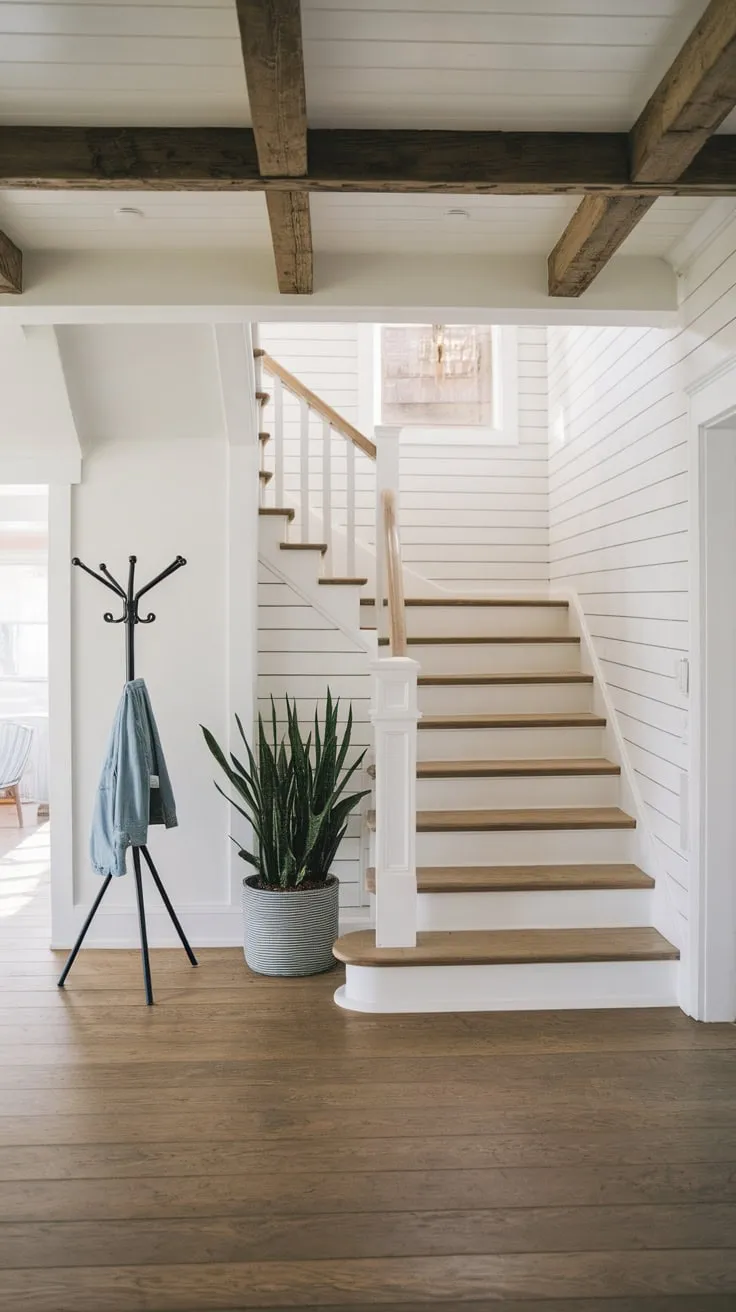A modern farmhouse foyer boasts a coastal-inspired entryway with wooden stairs, exposed beams, and a welcoming blend of rustic and clean aesthetics.