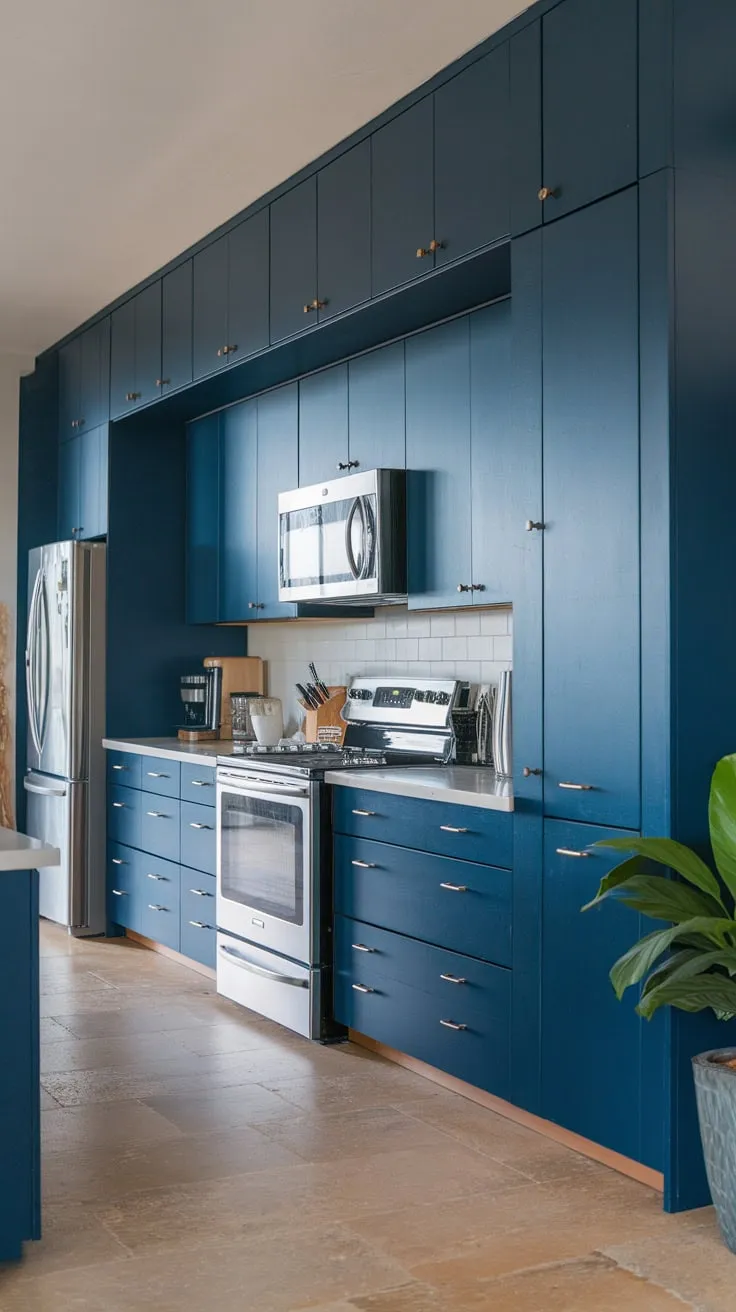 Sleek dark blue cabinetry dominates a modern kitchen's open design, complemented by white countertops and beige tile flooring
