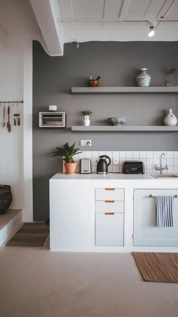 Bright lighting illuminates a sleek modern minimalist kitchen featuring a white countertop, grey walls, and carefully curated minimalist décor.