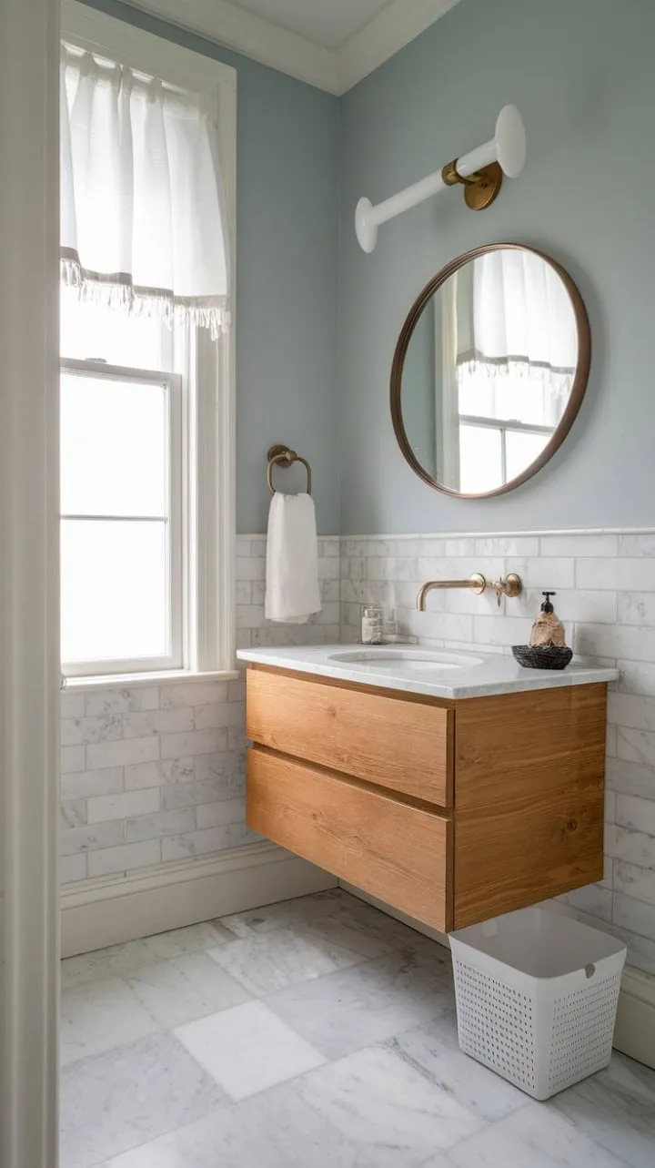 This compact powder room blends minimalist design with luxurious details, featuring calming light blue walls, an oak vanity, and elegant white marble and bronze accents.