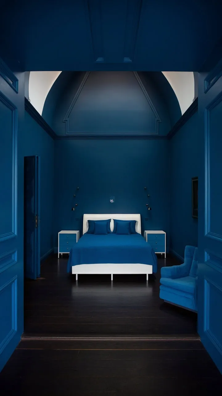 In a serene sanctuary of deep indigo and minimalist design, a dramatic overhead light accentuates the crisp white bedding, creating a tranquil oasis of calm.