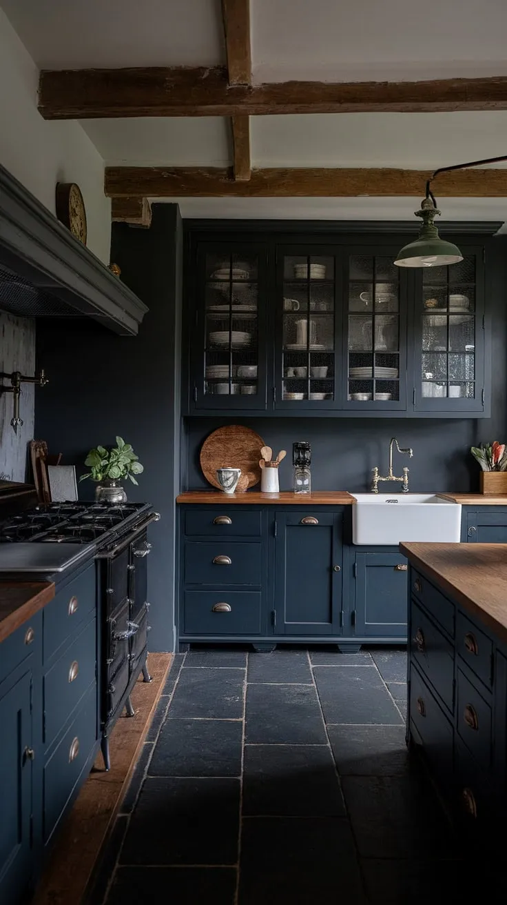 This moody farmhouse kitchen features dark grey and black cabinets, a classic design with a vintage stove, and rustic charm from exposed beams and a vintage light fixture.