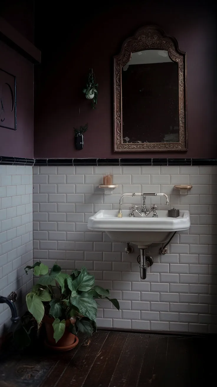 The dark boho bathroom showcases a vintage mirror, dark wood flooring, and a potted plant, perfectly blending elements of dark academia and moody aesthetics.