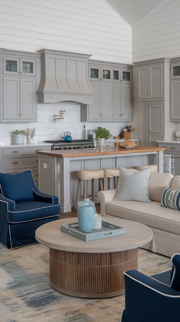 This dreamy coastal farmhouse kitchen and living area is the epitome of relaxed elegance. The gray cabinets and white shiplap create a bright and airy feel, while the wooden island with its integrated sink and stove provides both functionality and a central gathering point. The adjacent living space, with its comfortable seating and beach-themed rug, offers a welcoming atmosphere perfect for unwinding after a day by the sea. A truly inspiring space.