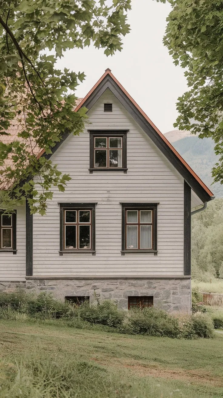 A pristine white Nordic house with black trim, nestled in a verdant landscape against a majestic mountain backdrop, showcases classic Scandinavian design.